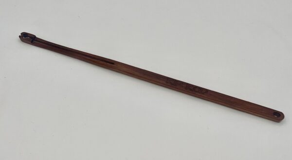A long, slender wooden stick engraved with "Ipe," featuring a small notch and hole at one end, rests on a plain white surface.