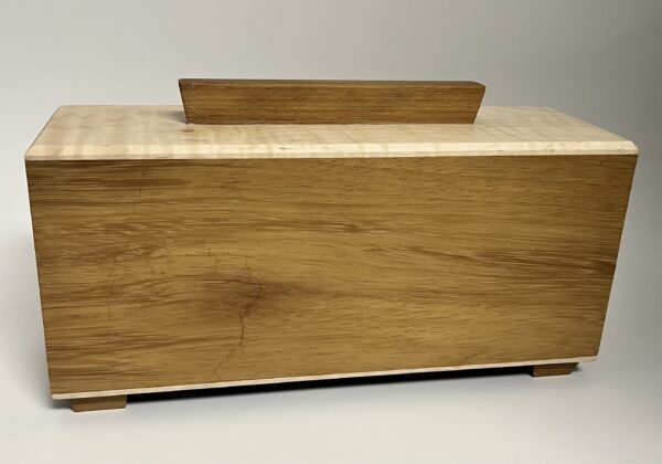 The Hideaway is a rectangular wooden box with a smooth, light brown finish, featuring a flat lid with a central handle and four small feet, set against a plain background.