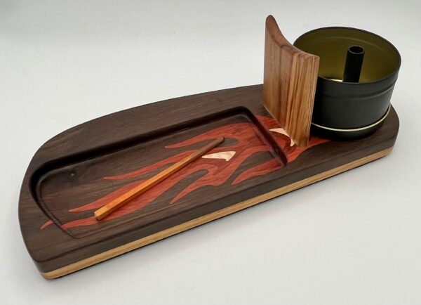 The Roadster Flame features a wooden tray with a flame motif, holding two chopsticks, a lidded container, and a vertical divider, all set against a light background.