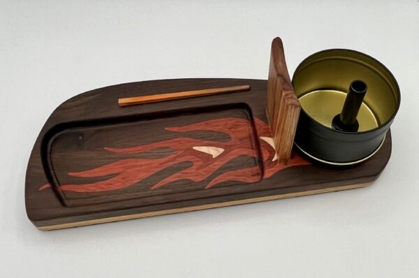 The Roadster Flame is a wooden tray with a red and orange flame inlay, featuring a slot for a stick and a round metal ashtray with a black center, separated by a vertical wood divider.