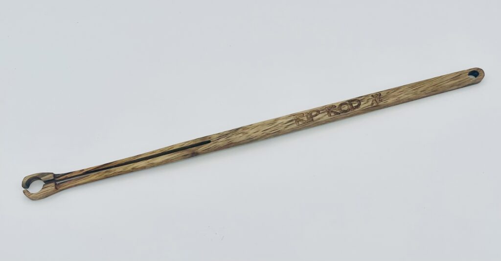 A long, wooden tool with a narrow handle and a small circular clamp at one end, featuring the word "PRODYNE" engraved on the side, displayed on a plain white background.