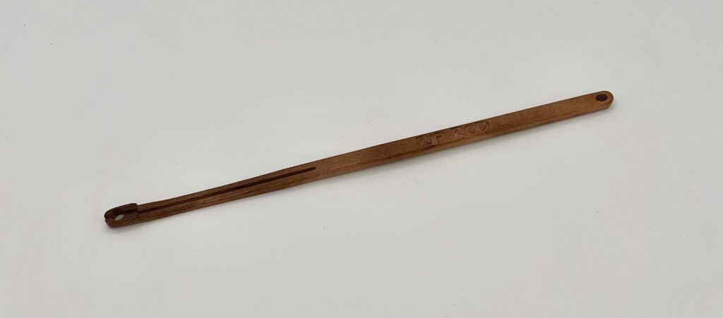 The Tigerwood is a long, slender wooden tool featuring a split end and a small circular hole at the opposite end, shown on a plain white background.