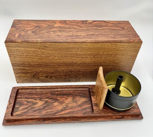 A wooden box with a sliding lid, displayed open to reveal a metal tin with a central handle inside. The box and lid have a rich, reddish wood grain pattern.