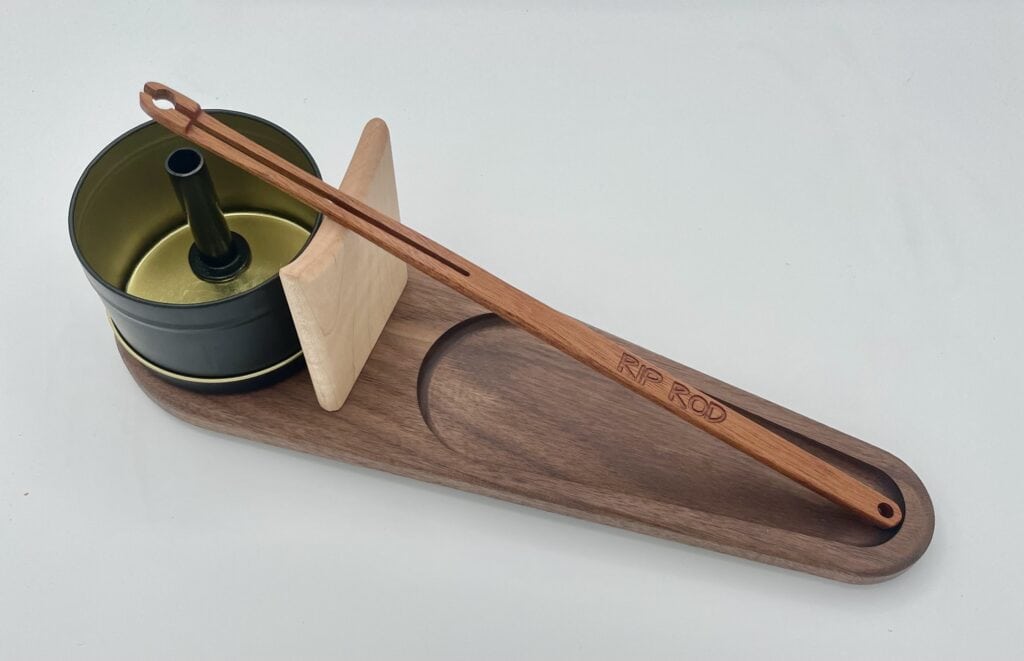 The Rip Rod Essentials set features a wooden tray holding a metal tin with a black center, a light wood paddle, and a long engraved "RIP ROD" rod, all neatly arranged on a white surface.