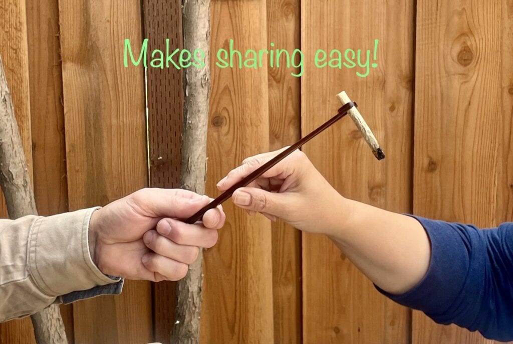 Two hands reach toward each other; one hand holds a chopstick with a rolled joint at the end. Green text above reads, "Makes sharing easy!" A wooden fence is in the background.